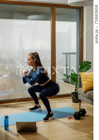 Woman in tracksuit in squat position by panoramic window  75880608