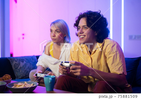 Happy young couple playing and winning a game funny activity sitting home on a sofa 75881509