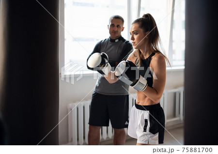 Father is preparing his young daughter for mixed martial arts competitions. The girl hits a punching bag Father is preparing his young daughter for mixed martial arts competitions. The girl hits a punching bag 75881700
