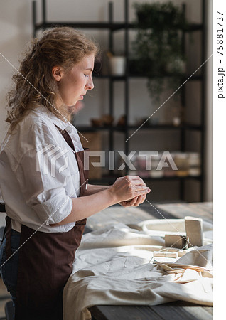 A young potter woman making pot in her own working place. Standing in spacious studio creating the shape of the future product with her hands. A young potter woman making pot in her own working place. Standing in spacious studio creating the shape of the future product with her hands. 75881737