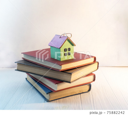 A stack of books or textbooks with a small decorative house with space for text. The concept of home education. 75882242