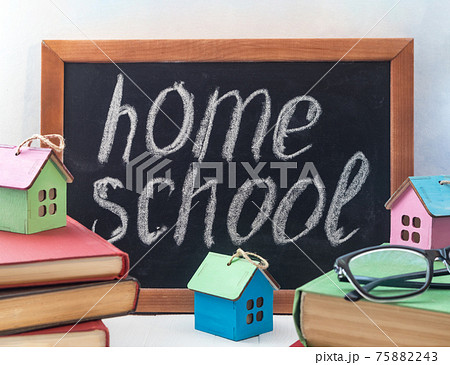 A stack of books or textbooks with a small decorative house and a blackboard with space for text. The concept of home education. 75882243