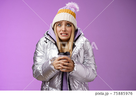 Shaking uncomfortable displeased girl wearing stylish silver jacket hat trembling freezing cold warm hands holding take-away coffee cup clench teeth pop eyes discomfort, standing purple background 75885976