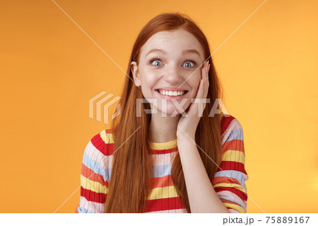 Cheerful glad excited attractive redhead girl blushing surprised feeling happy touch cheek pleased receive good news standing joyful thrilled get awesome chance, posing orange background 75889167