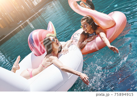 The best way to relax! Two beautiful happy and young women in swimwear enjoying summer day while floating in the pool. The best way to relax! Two beautiful happy and young women in swimwear enjoying summer day while floating in the pool. 75894915