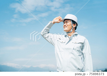 青空と作業服を着た男性 75896373