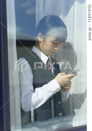 窓辺でスマートフォンを見る中学生（外出自粛要請のイメージ） 75897950
