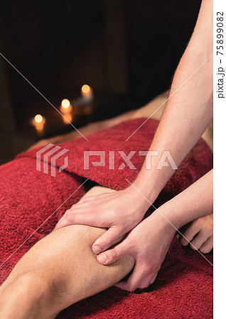 Close-up Masseur man doing thigh massage of the leg to a man athlete client in a dark room of a massage spa Close-up Masseur man doing thigh massage of the leg to a man athlete client in a dark room of a massage spa 75899082