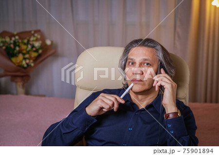 A 50-year-old man speaks on the phone at home, sitting in a chair. Relaxing delight. A 50-year-old man speaks on the phone at home, sitting in a chair. Relaxing delight. 75901894