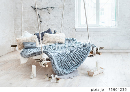 White loft interior in classic scandinavian style. Hanging bed suspended from the ceiling. Cozy large folded gray plaid, giant knit blanket, super chunky yarn, arm knitting. Trendy room design. White loft interior in classic scandinavian style. Hanging bed suspended from the ceiling. Cozy large folded gray plaid, giant knit blanket, super chunky yarn, arm knitting. Trendy room design. 75904236