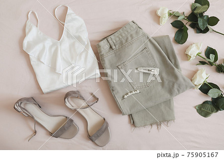 Overhead view of woman's casual spring summer outfit. Jeans, white blouse, sandals and bouquet of flowers on beige background. Flat lay, top view. 75905167