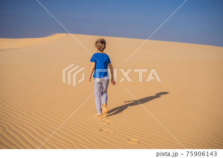 Young boy traveling in the desert. Sandy dunes and blue sky on sunny summer day. Travel, adventure, freedom concept. Tourism reopens after quarantine COVID 19 75906143
