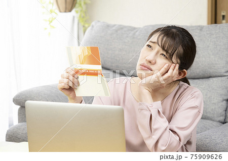預金通帳を見て悩む女性 預金通帳を見て悩む女性 75909626