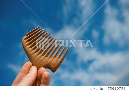 A hand holding natural wooden comb made of pear tree for scalp massage and aroma combing A hand holding natural wooden comb made of pear tree for scalp massage and aroma combing 75910721