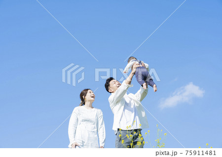 青空のもと、赤ちゃんを高く抱き上げる父母 青空のもと、赤ちゃんを高く抱き上げる父母 75911481