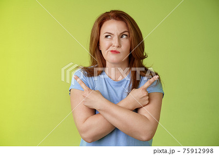 Time make right choice. Perplexed hesitant redhead middle-aged female customer deciding between few variants cross arms body pointing sideways look left smirking unsure doubting choosing product Time make right choice. Perplexed hesitant redhead middle-aged female customer deciding between few variants cross arms body pointing sideways look left smirking unsure doubting choosing product 75912998