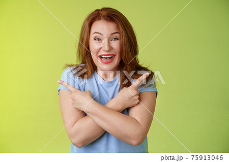 Happy carefree entushiastic redhead funny mature female having fun positive attitude cross arms body pointing sideways show left right products laughing happily like both choices green background Happy carefree entushiastic redhead funny mature female having fun positive attitude cross arms body pointing sideways show left right products laughing happily like both choices green background 75913046