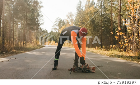 Training an athlete on the roller skaters. Biathlon ride on the roller skis with ski poles, in the helmet. Autumn workout. Roller sport. Athlete is getting ready to start. Training an athlete on the roller skaters. Biathlon ride on the roller skis with ski poles, in the helmet. Autumn workout. Roller sport. Athlete is getting ready to start. 75919297