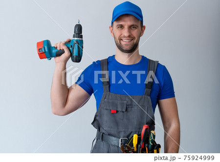 Uniformed maintenance worker holds a screwdriver and looks at the camera. Handyman wearing a tool belt Uniformed maintenance worker holds a screwdriver and looks at the camera. Handyman wearing a tool belt 75924999