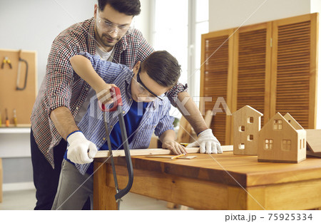 Father teaching son use sharp handsaw for woodworking at home carpentry workshop Father teaching son use sharp handsaw for woodworking at home carpentry workshop 75925334
