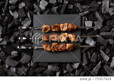 kebab on skewers. Three portions of grilled meat on a stone plate. Charcoal background. Top view. 75927828