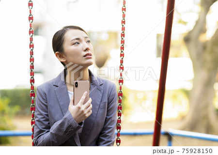 公園でたそがれる若い女性　スーツ　スマホ 75928150