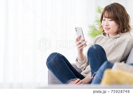 ソファでスマホのSNSのメッセージを読みながらリラックスする女子学生 ソファでスマホのSNSのメッセージを読みながらリラックスする女子学生 75928749