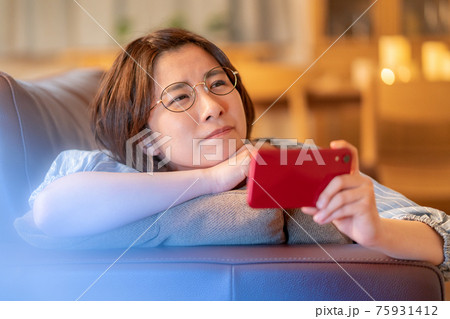 自宅のリビングのソファでスマホを見て悩む若い女性 75931412