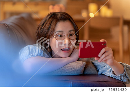 自宅のリビングのソファでスマホを見て若い女性 自宅のリビングのソファでスマホを見て若い女性 75931420