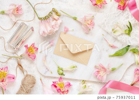 Beige envelope on a white table between pink flowers 75937011