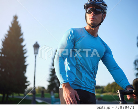 Portrait of professional young male biker in sportswear, protective helmet and glasses looking away while standing with his bike, training in park on a daytime 75939471