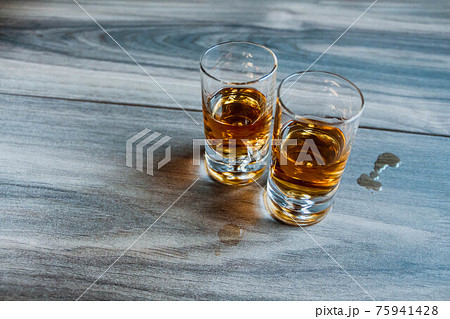Two shot glasses with whiskey on a wooden background Two shot glasses with whiskey on a wooden background 75941428
