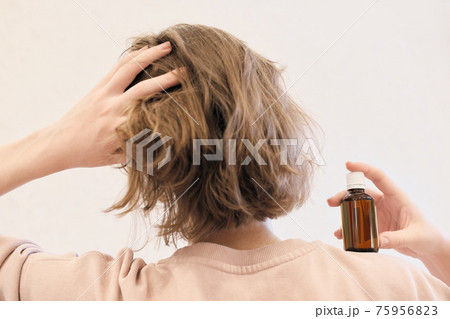 back view of a woman with hair oil bottle. woman touchinh her head and holding argan or coconut or avocado iol bottle. hair loss prevention and care routine. hydration and nourishing 75956823