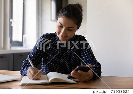 Close up focused Indian woman writing notes, holding phone Close up focused Indian woman writing notes, holding phone 75958624