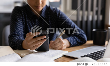 Close up Indian woman holding phone, writing notes, watching webinar 75958637