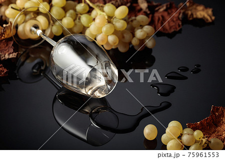 Glass of white wine with grapes and dried up vine leaves. 75961553