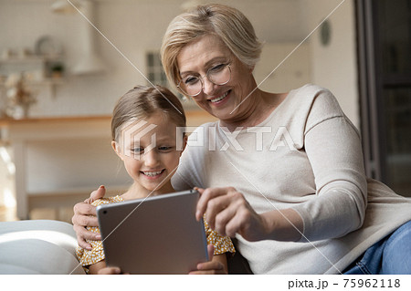 Smiling granny and small granddaughter use tablet 75962118