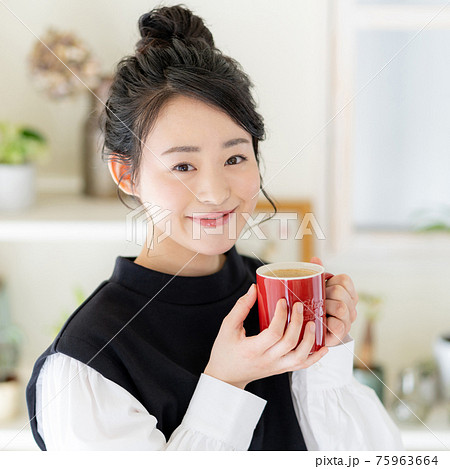 リビングで赤いマグカップでカフェオレを飲む若い女性 正方形 リビングで赤いマグカップでカフェオレを飲む若い女性 正方形 75963664
