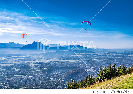 Paragliding over Salzburg in Austria, Europe. Two paragliders, seen from 1287 meters high Gaisberg mountain, with view of capital city of Salzburg, the fortress Hohensalzburg and vicinity. Photo. Paragliding over Salzburg in Austria, Europe. Two paragliders, seen from 1287 meters high Gaisberg mountain, with view of capital city of Salzburg, the fortress Hohensalzburg and vicinity. Photo. 75965748