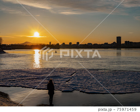 A girl on the shore at sunset is waiting for the fishermen. Winter shooting. Cityscape. 75971459