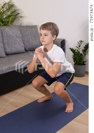 Blond boy goes in for sports on yoga mat. Child physical activity squat exercise at home. Blond boy goes in for sports on yoga mat. Child physical activity squat exercise at home. 75973874