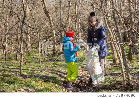 A girl throws a plastic bottle into a trash bag that the girl holds, together they collect garbage in the forest A girl throws a plastic bottle into a trash bag that the girl holds, together they collect garbage in the forest 75974090