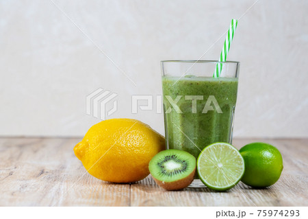 Tall glass with kiwi and spinach smoothie surrounded by fruits on a wooden table 75974293