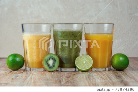 Three tall glass with kiwi and spinach smoothies in a row surrounded by fruits 75974296