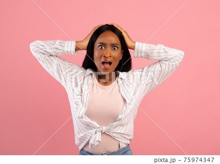 Unbelievable news. Emotional black woman holding her head in shock over pink studio background Unbelievable news. Emotional black woman holding her head in shock over pink studio background 75974347