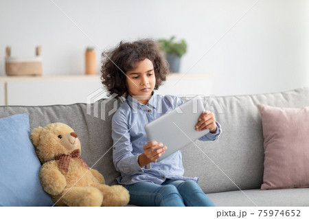 Afro girl using digital tablet, sitting on the couch Afro girl using digital tablet, sitting on the couch 75974652
