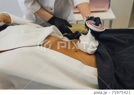 Woman in special white suit getting anti cellulite massage in a spa salon. LPG, and body contouring treatment in clinic. 75975421