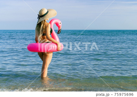 Summer time. Young sexy woman in straw hat, bikini swimsuit, sunglasses with pink inflatable flamingo in blue ocean water. Swimming water, having fun and enjoying travel vacation. Summer time. Young sexy woman in straw hat, bikini swimsuit, sunglasses with pink inflatable flamingo in blue ocean water. Swimming water, having fun and enjoying travel vacation. 75975696