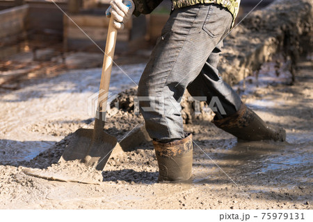 Raking concrete. Concrete for parking lot construction. A worker in boots flattens the concrete with a shovel. 75979131