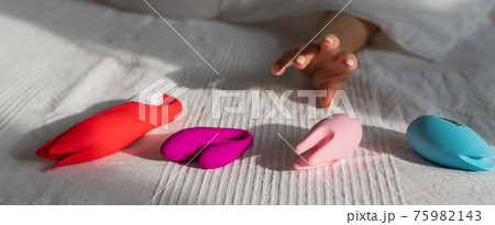 The woman lies in bed under a white blanket and reaches for the vibrators. Girl and sex toys in the bedroom 75982143